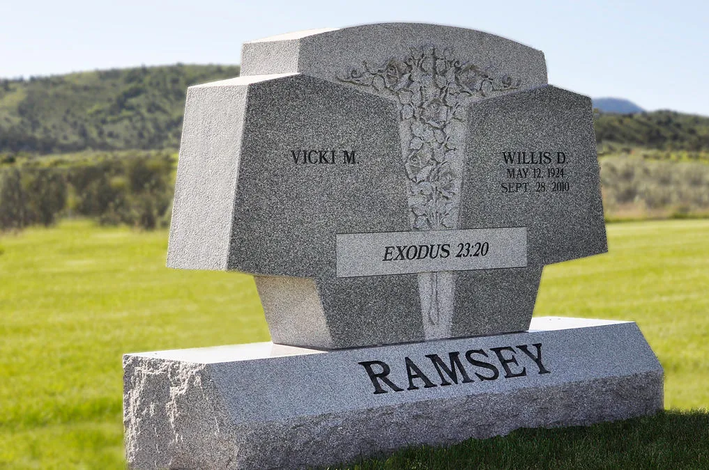 A custom cross-shaped memorial in light granite on a rough-hewn base.